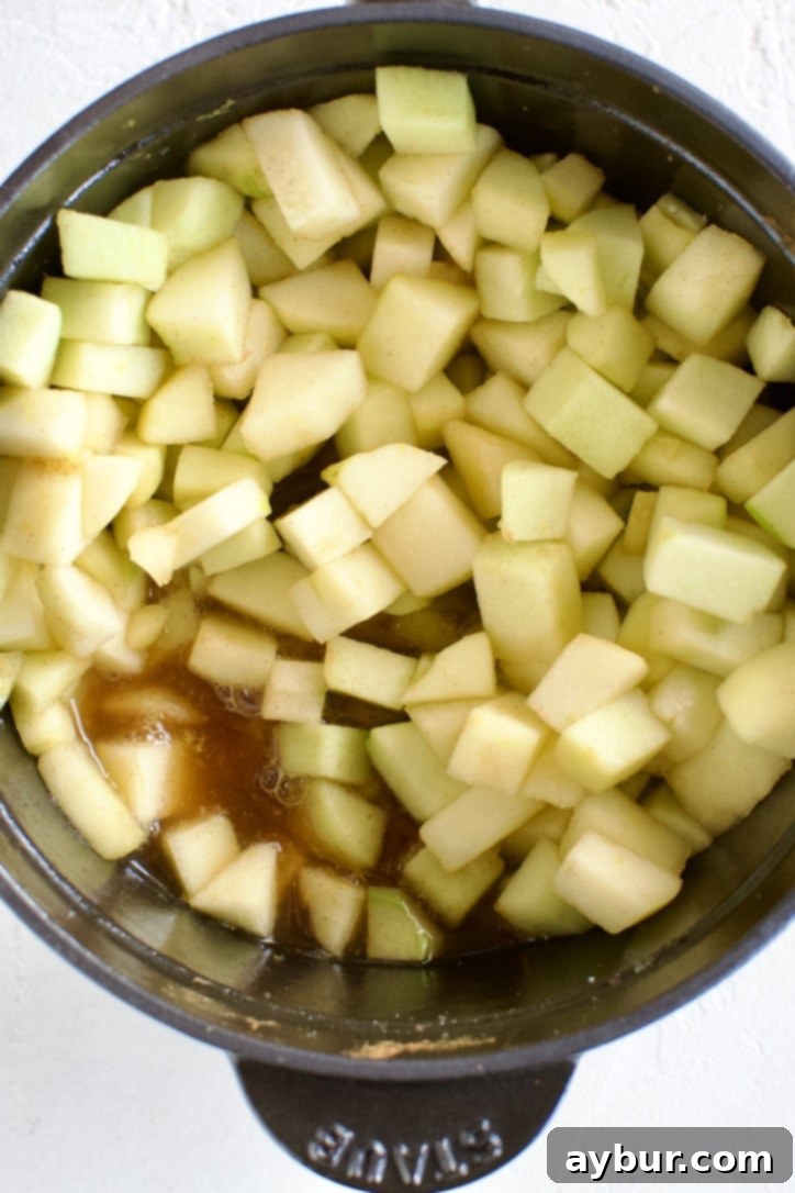 The applesauce ingredients in the pot are thoroughly stirred together, ensuring everything is well combined before heating.