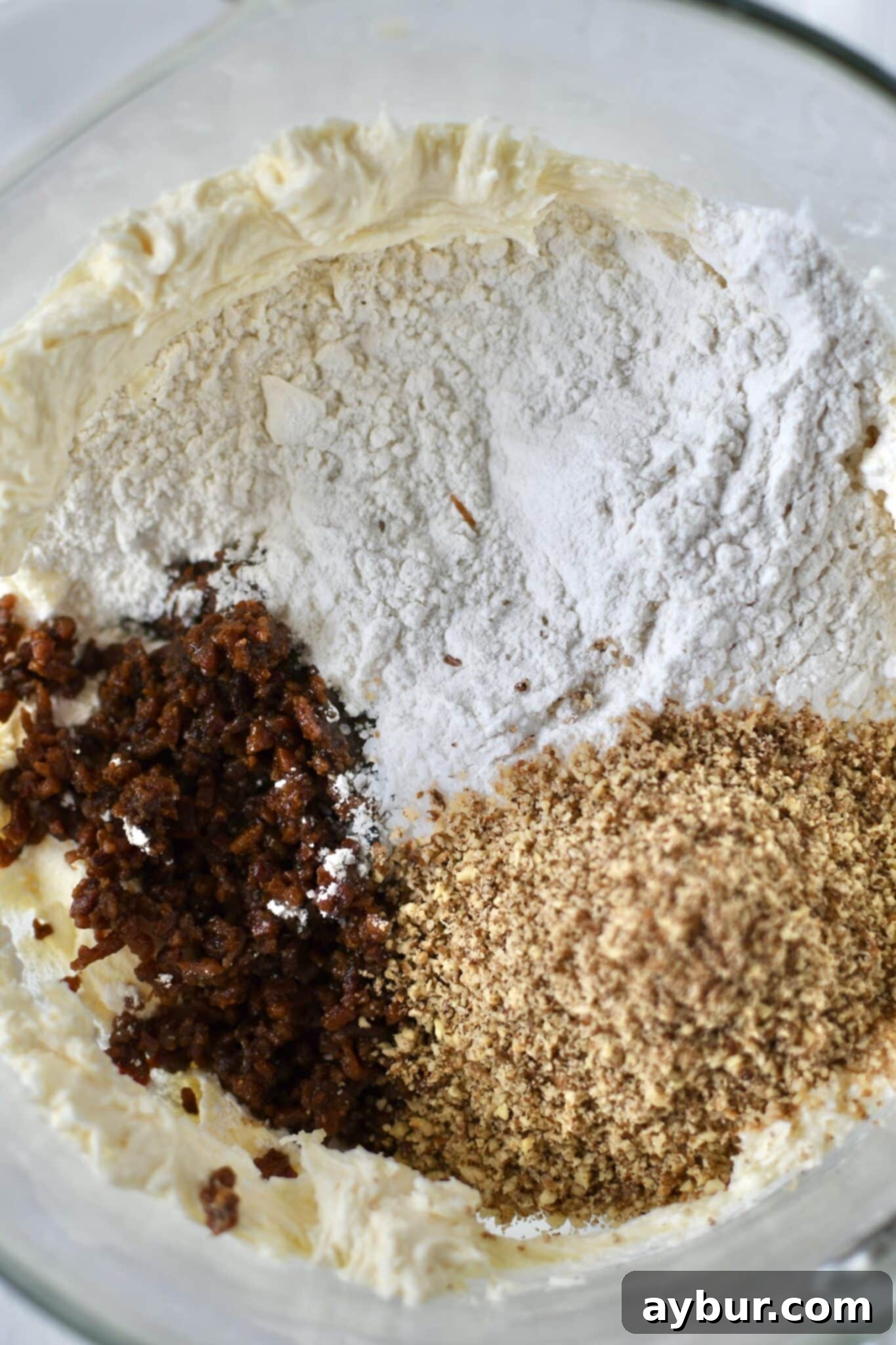 Adding all-purpose flour, finely chopped bacon, kosher salt, and toasted pecans to the creamed butter and maple mixture.