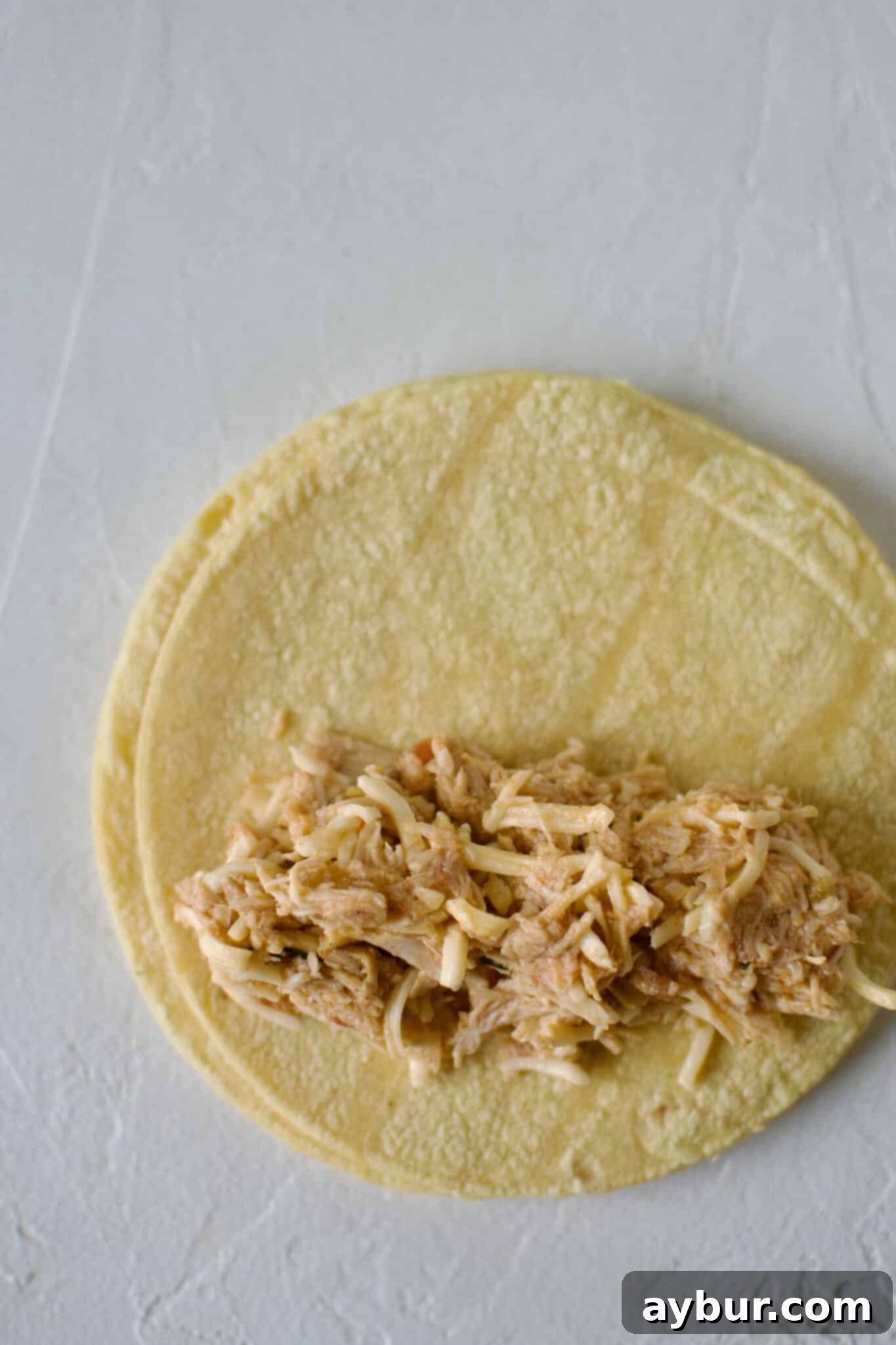 Filling a corn tortilla with mexican shredded chicken and rolling up for enchiladas.
