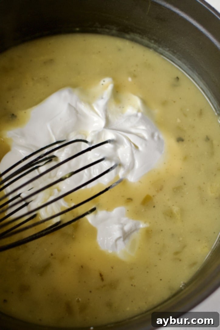 Velvety Sour Cream Enchilada Sauce 5 Sour cream being carefully added to the thickened enchilada sauce base.