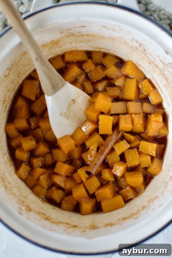 Pumpkin jam simmering in a saucepan, halfway through the cooking process, with ingredients softening.