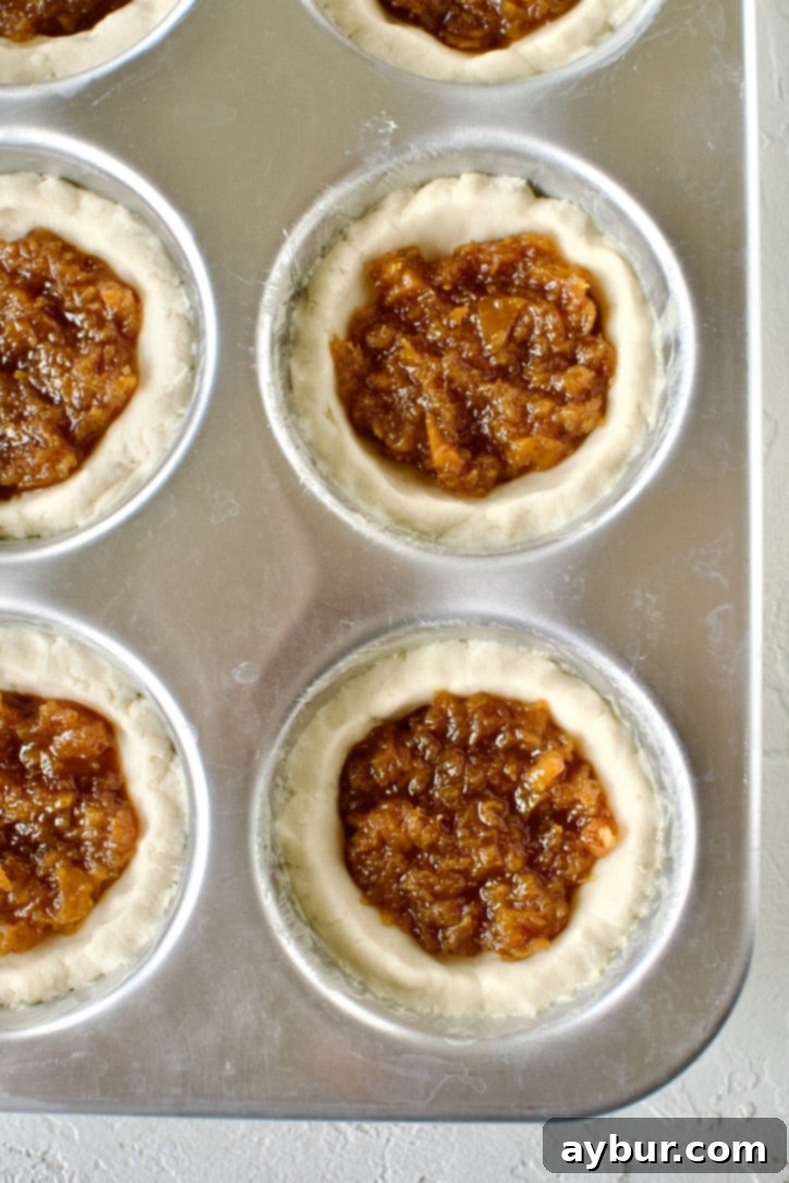 Spiced Pumpkin Delights 9 Pumpkin tartlets in a muffin tin, topped with crumbles of dough before baking.