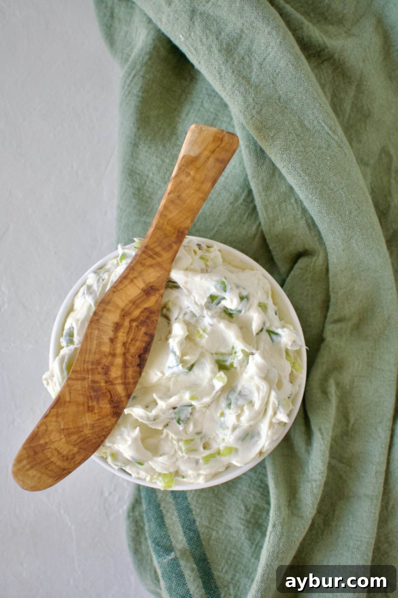 Finished scallion cream cheese in a dish ready to eat. With a wood spreading knife resting on the side.