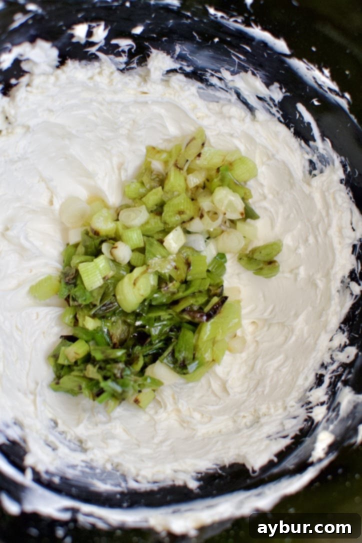 Adding the cooked and chopped scallions to the whipped cream cheese in the stand mixer bowl.