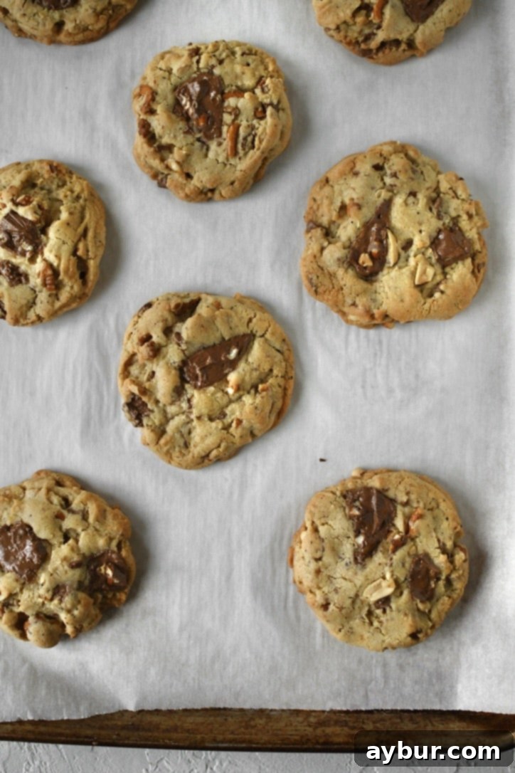 Freshly baked kitchen sink cookies on a parchment-lined baking sheet, golden brown with melted chocolate.