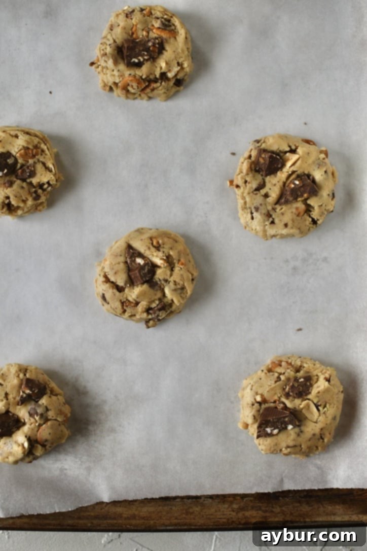 Raw cookie dough portions with extra chocolate chunks on top, arranged on a baking sheet before baking.