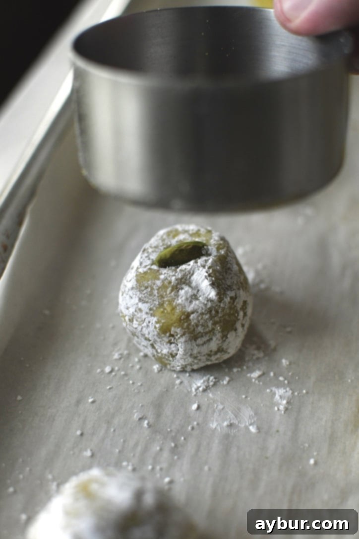 The bottom of a measuring cup hovering over a sugared amaretti cookie, poised to gently flatten it.