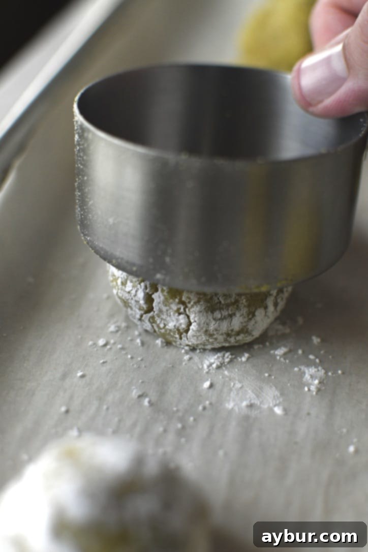 A measuring cup gently pressing down on an amaretti cookie, slightly flattening its top.