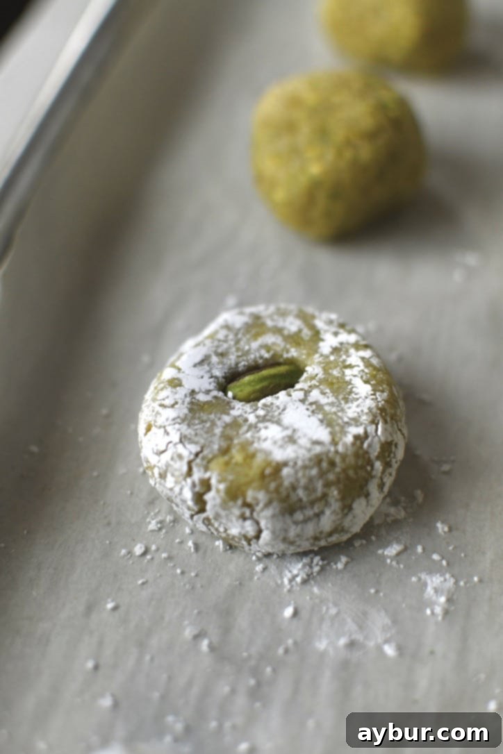 A perfectly shaped amaretti cookie, gently flattened and topped with a pistachio halve, ready for baking.