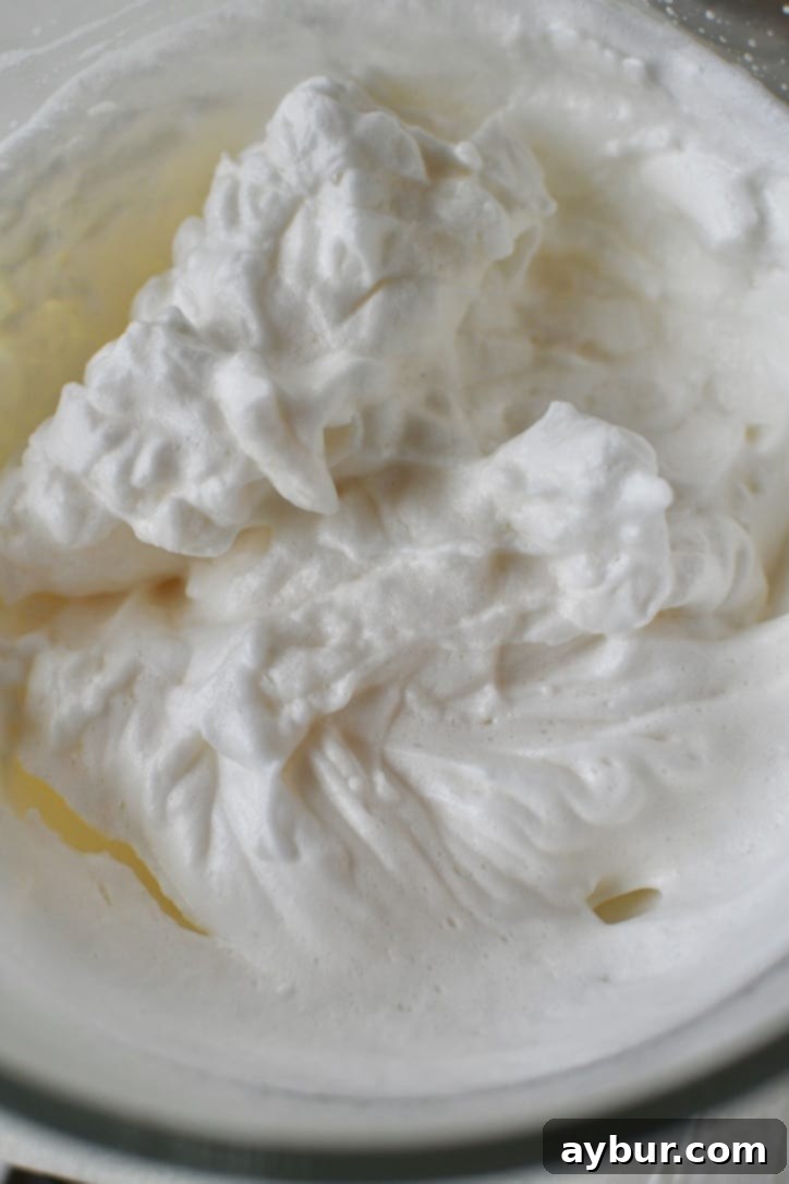 Perfectly whipped egg whites in a mixing bowl, showcasing stiff peaks after vanilla and almond extracts have been incorporated.