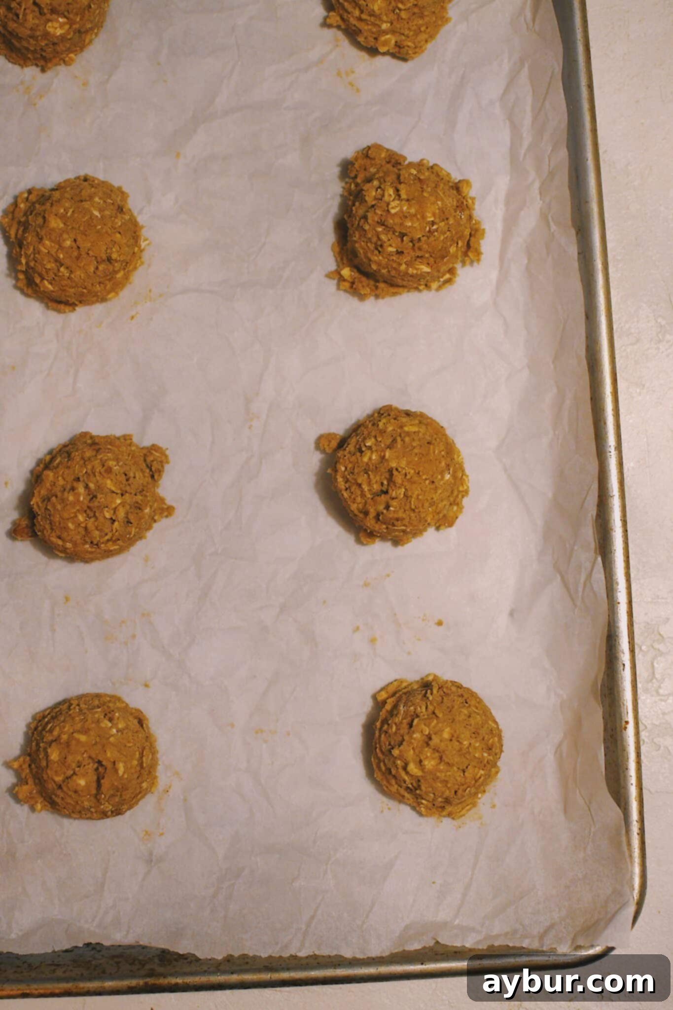 Festive Gingerbread Oatmeal Cream Pies 7 Portioned gingerbread oatmeal cookie dough balls, neatly arranged and chilled on a parchment-lined sheet pan, ready for baking.