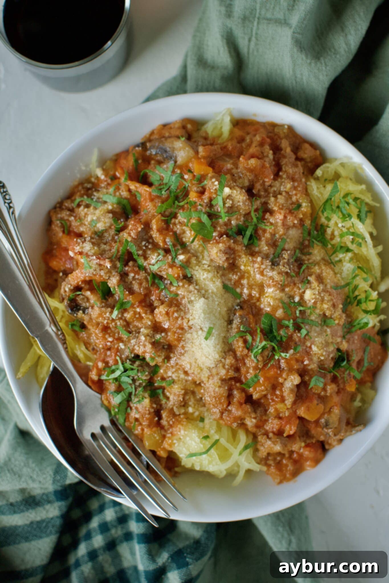 A vibrant bowl of Sausage Bolognese served over perfectly roasted spaghetti squash, garnished with generous shavings of Parmesan cheese and fresh basil leaves, ready to be enjoyed.