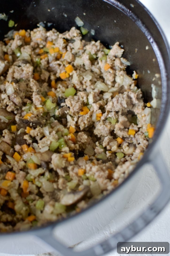 The same pot now contains the cooked vegetables and garlic, with crumbled Italian sausage added and actively browning, ensuring no pink remains and developing rich, savory flavors.