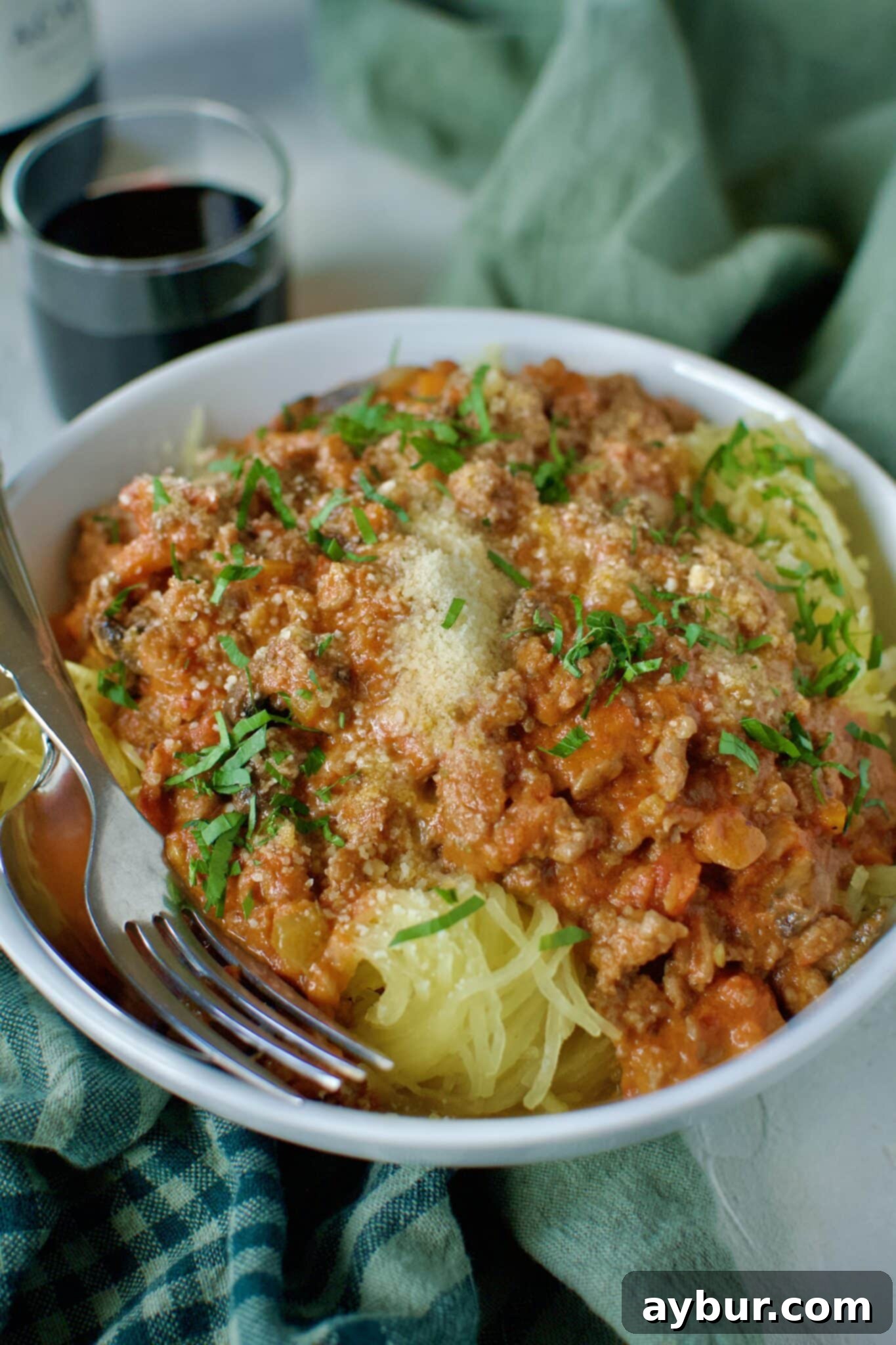 A delectable serving of creamy Sausage Bolognese generously ladled over roasted spaghetti squash strands, beautifully topped with a sprinkle of fresh Parmesan cheese and vibrant green basil leaves, presented for a mouthwatering meal.