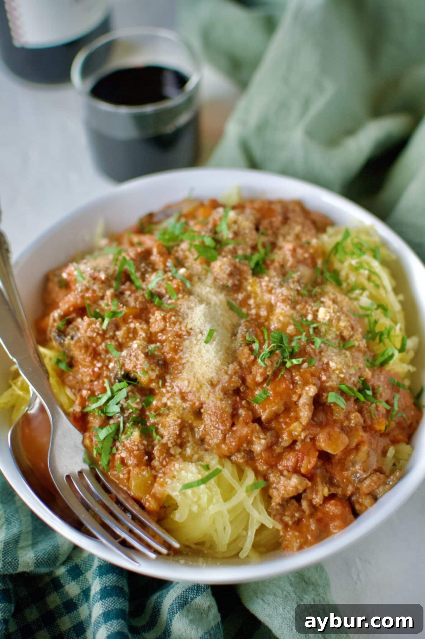 A close-up of a generous serving of Sausage Bolognese nestled over roasted spaghetti squash, elegantly finished with grated Parmesan and fresh basil leaves, highlighting the rich texture and vibrant colors.