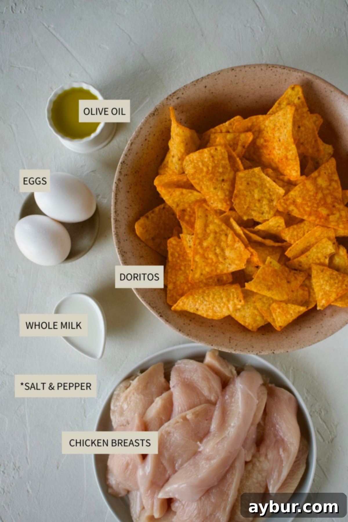 Ingredients needed to make Dorito Chicken including chicken breasts, eggs, milk, a bag of Doritos, and olive oil.