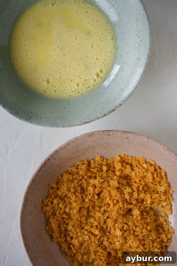 A shallow bowl of finely crushed Dorito crumbs next to another shallow bowl with beaten eggs and milk, prepared for breading chicken.