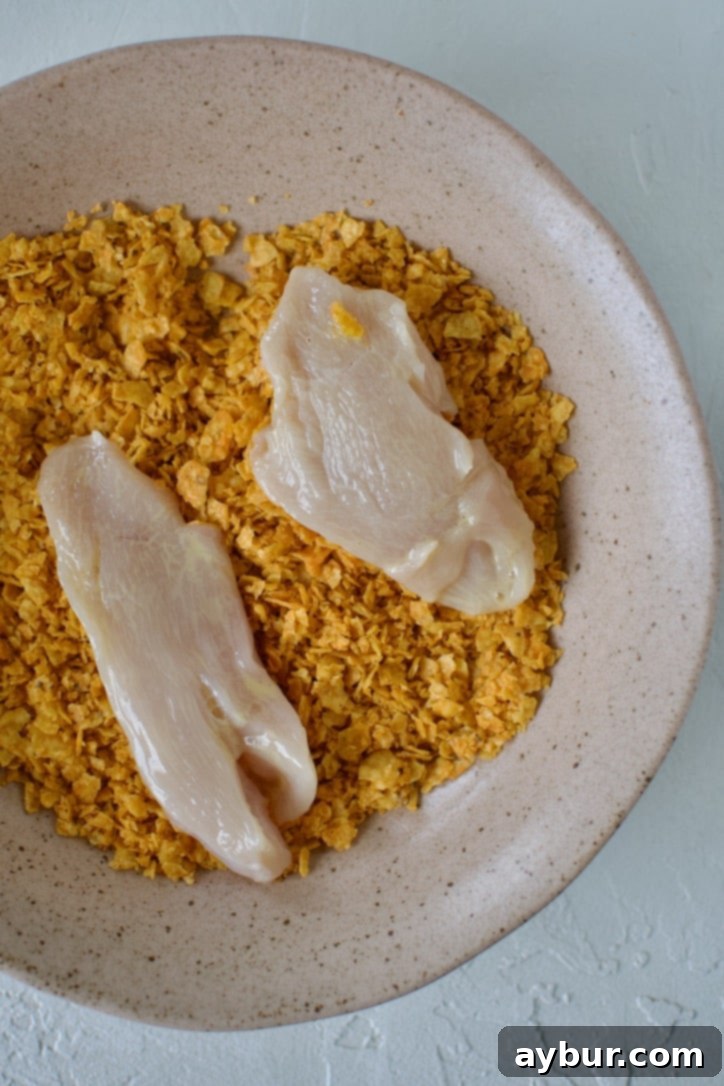 A close-up shot of chicken tenders being rolled and pressed into a bowl of Dorito crumbs to create a crispy coating.
