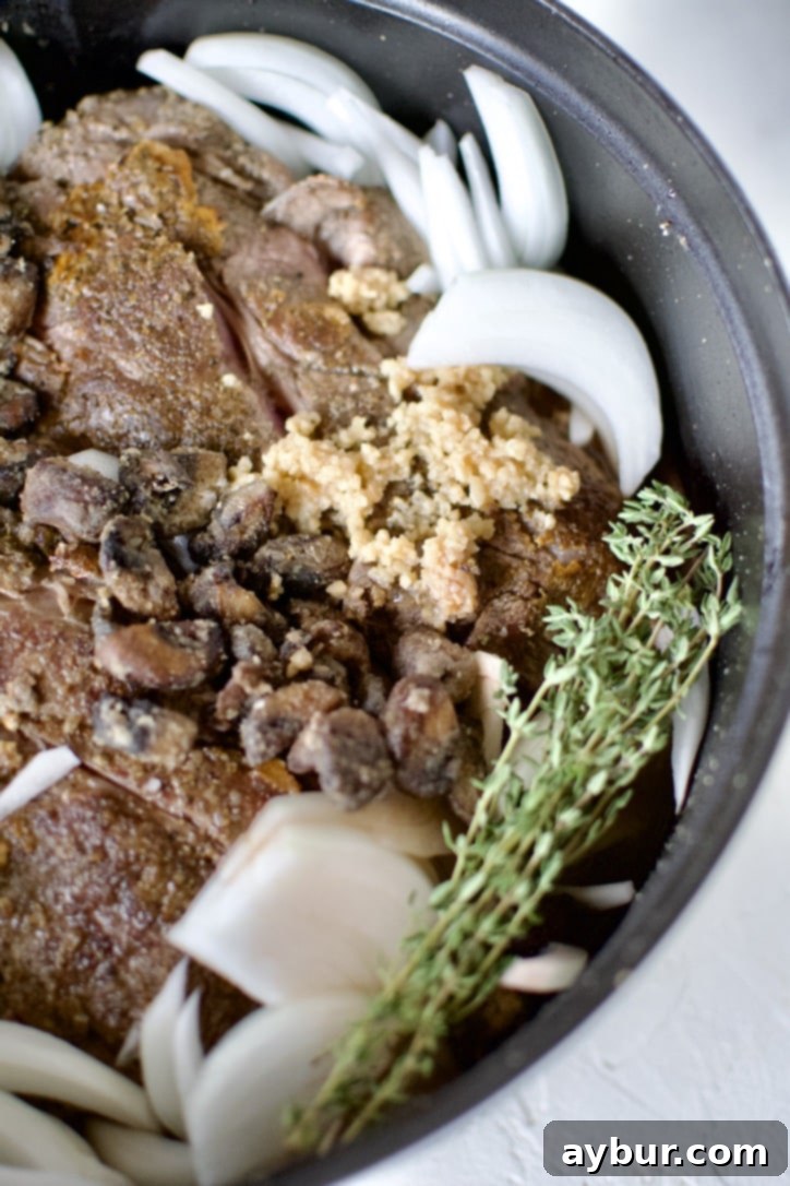 Seared chuck roast in a large pot with onions, cooked mushrooms, garlic, thyme, red wine, and beef stock.