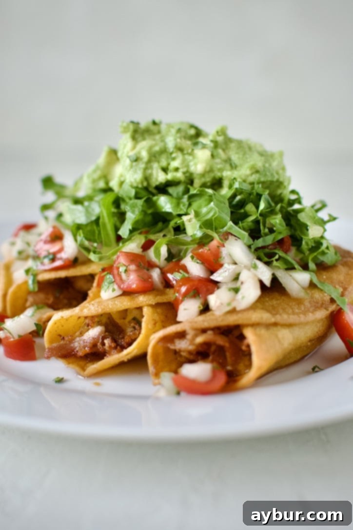 Flautas topped with pico de gallo, shredded lettuce, and avocado, ready to eat.