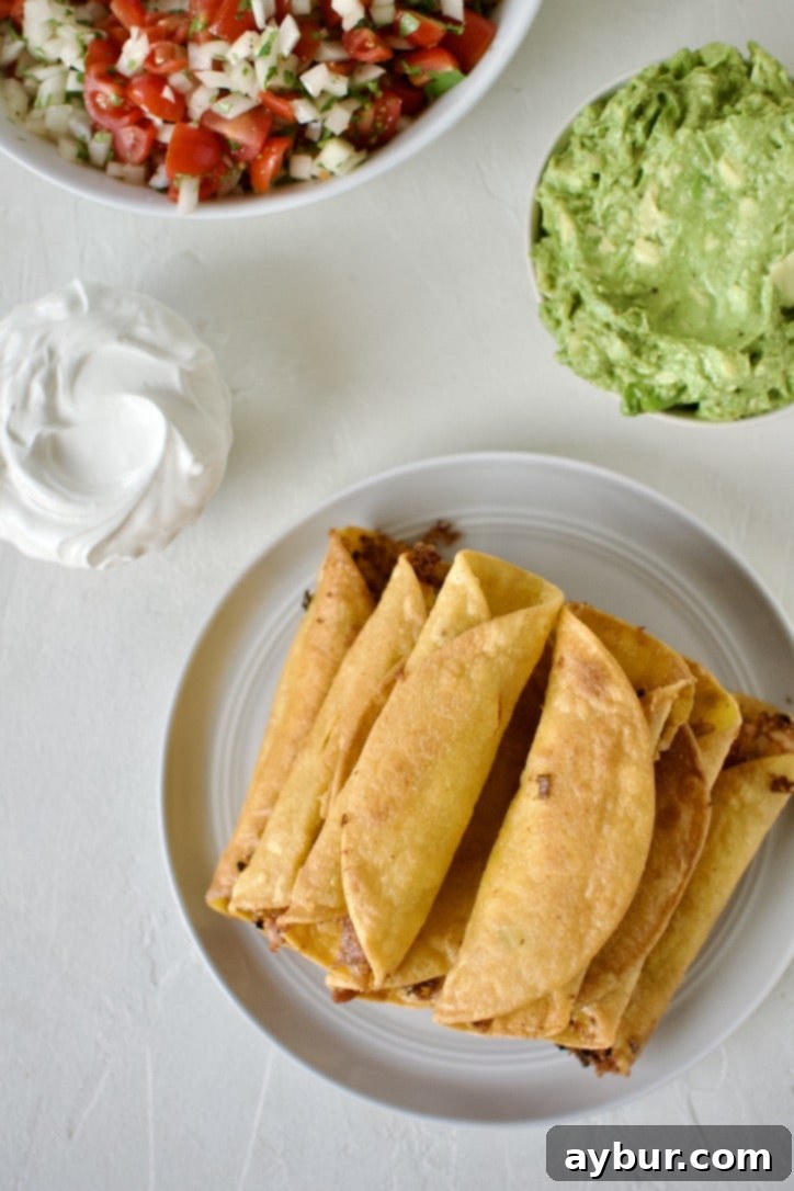 Cooked flautas stacked up on a plate cooling. Surrounded by optional toppings.