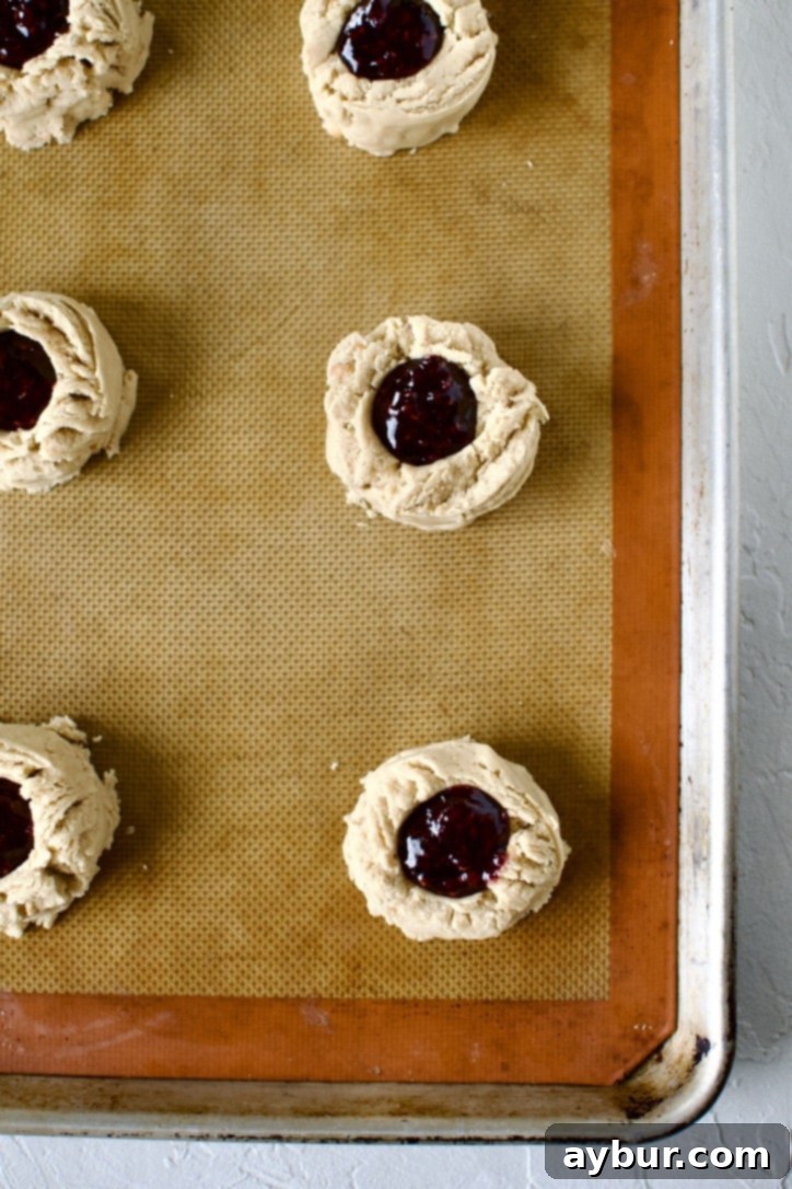 Peanut Butter Jelly Dream Cookies 9 Portioned cookies on a sheet pan with an indent made in them, filled with jelly.