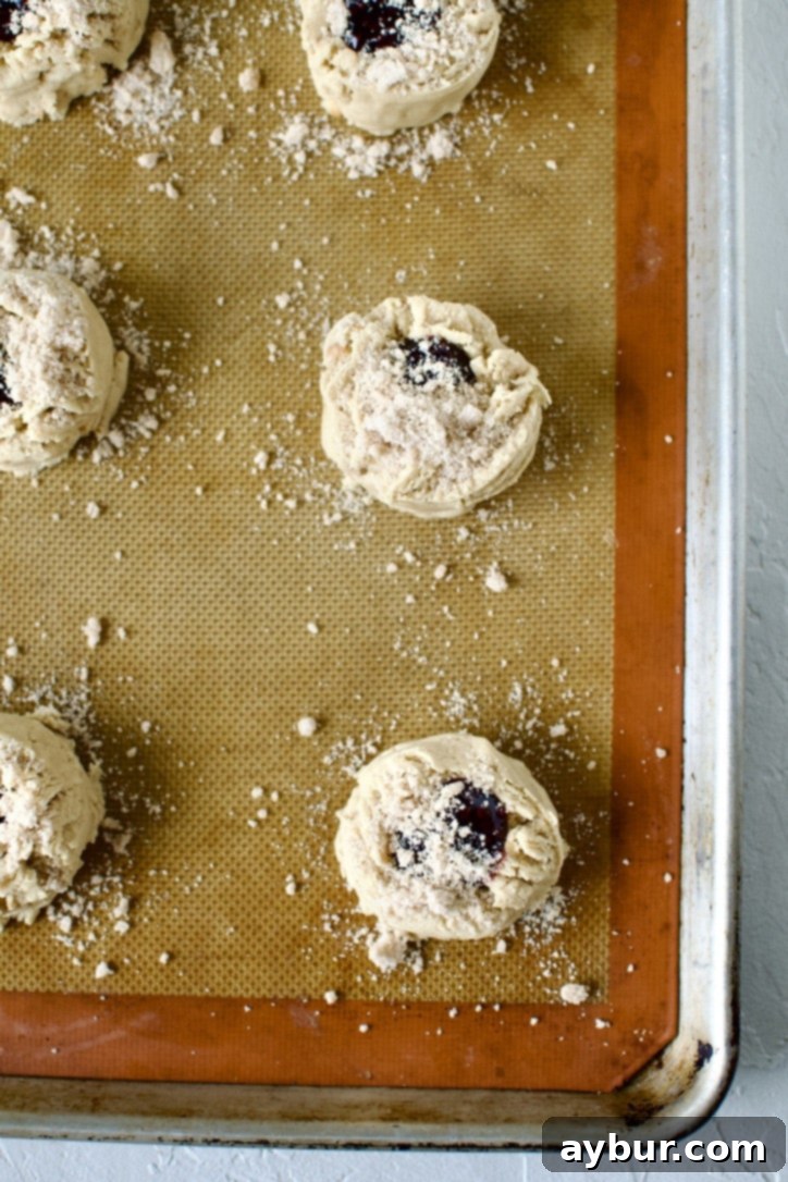 Peanut Butter Jelly Dream Cookies 10 Portioned cookies on a sheet pan with an indent made in them, filled with jelly and topped with crumble.