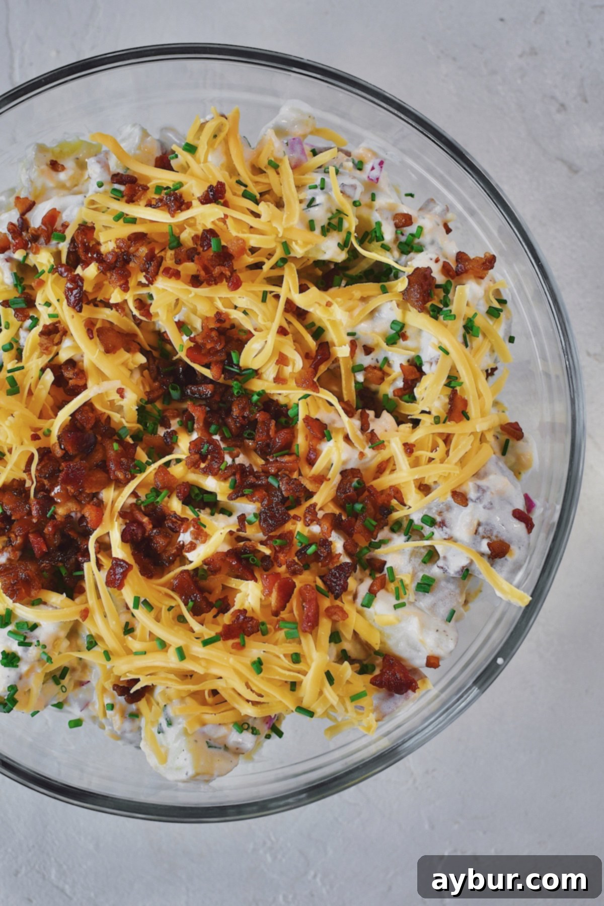 Ranch Potato Salad in a glass bowl topped with chives, bacon, and cheddar.