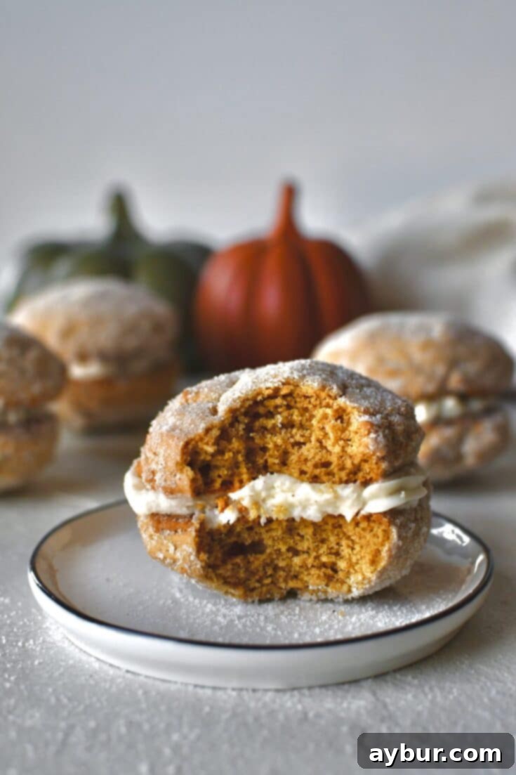 A Pumpkin Whoopie Pie on a plate with a bite taken out of it, surrounded by more whole pies.