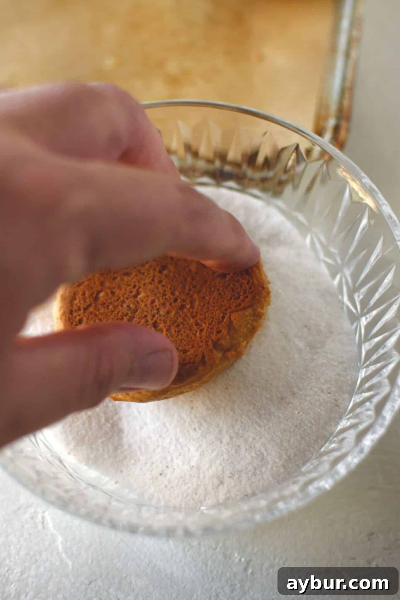 Buttered whoopie pie halves being dipped into a bowl of spiced sugar, ensuring a generous coating.