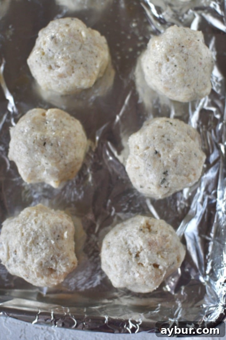 Flavorful Parmesan Chicken Meatballs 7 Perfectly rolled Parmesan Chicken Meatballs, spaced on a baking sheet.