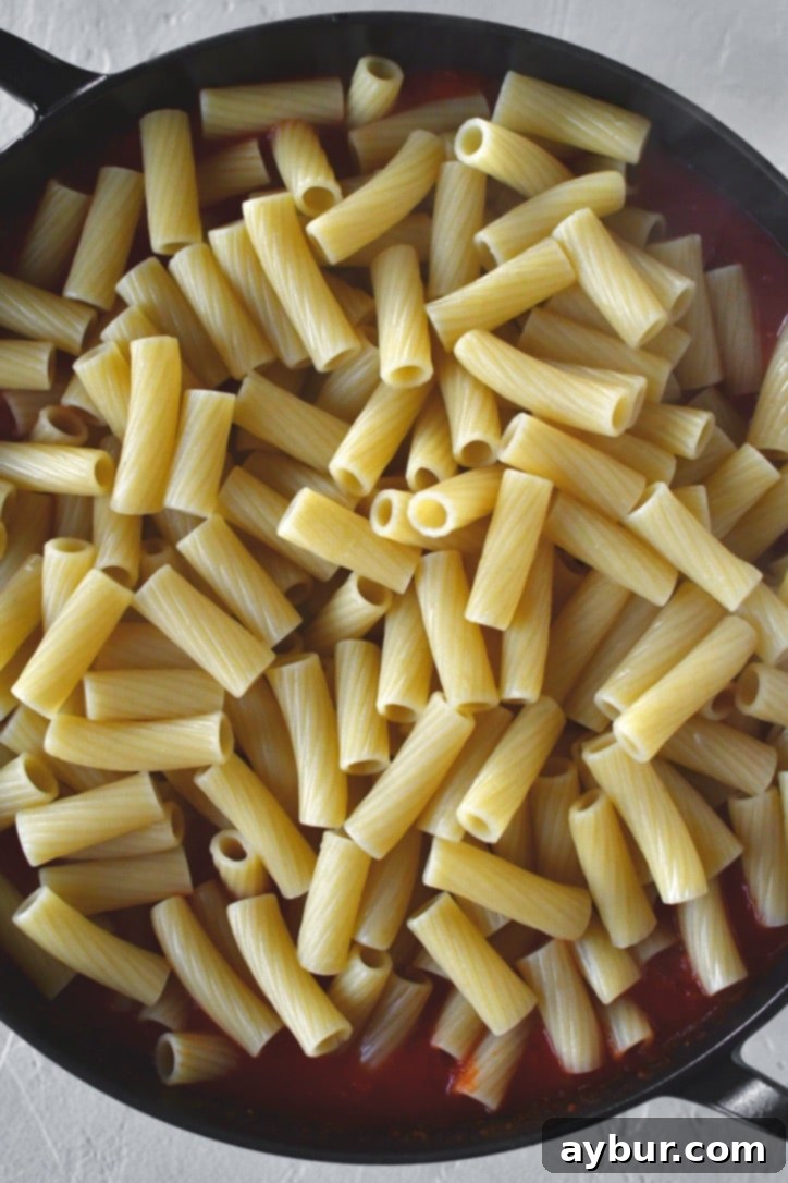 Flavorful Parmesan Chicken Meatballs 8 Baked chicken meatballs being added to marinara sauce and pasta in an oven-safe skillet.