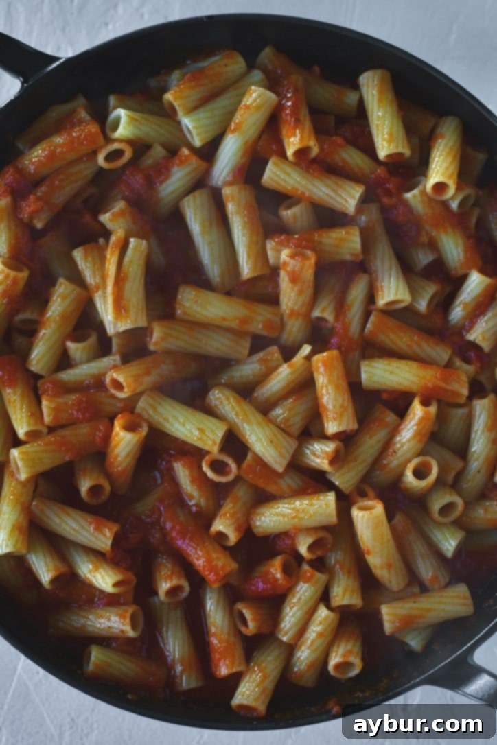 Flavorful Parmesan Chicken Meatballs 9 Tossing cooked rigatoni pasta with rich marinara sauce in a large pan.