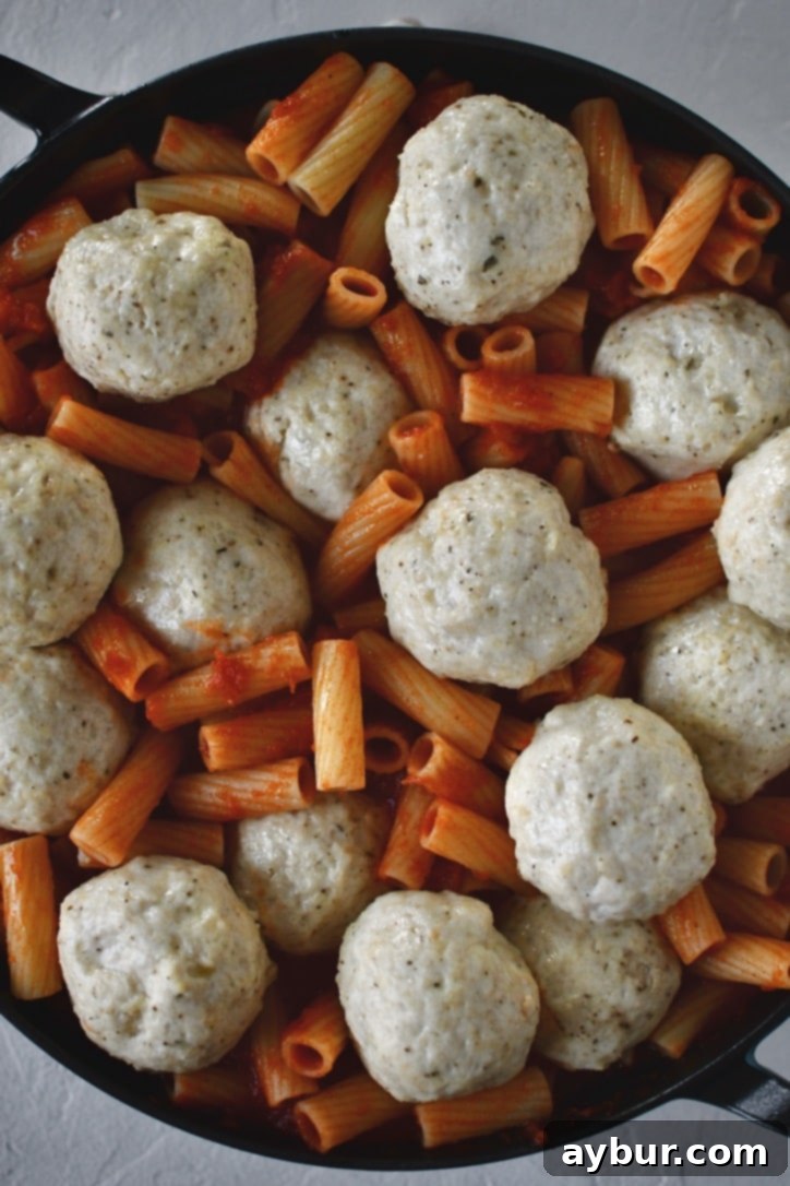 Flavorful Parmesan Chicken Meatballs 10 Cooked chicken meatballs nestled on top of pasta with marinara sauce, ready for cheese.