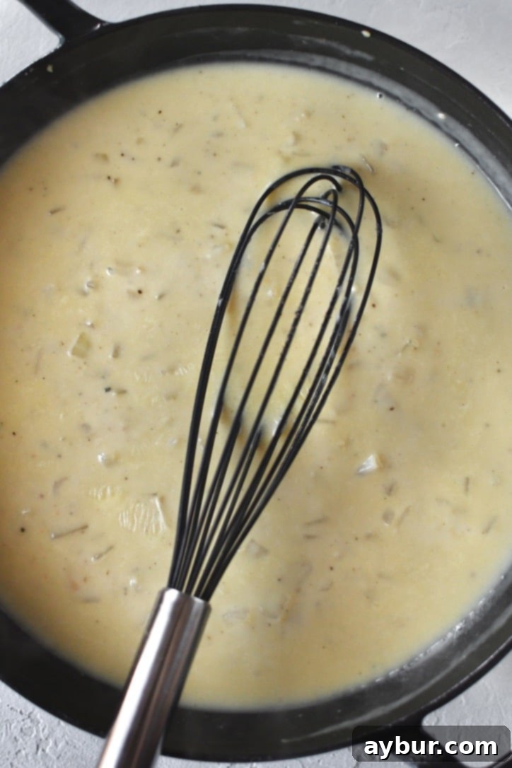 Golden Chicken Mash Bake 6 Chicken stock being whisked into a roux, forming a smooth, creamy sauce.