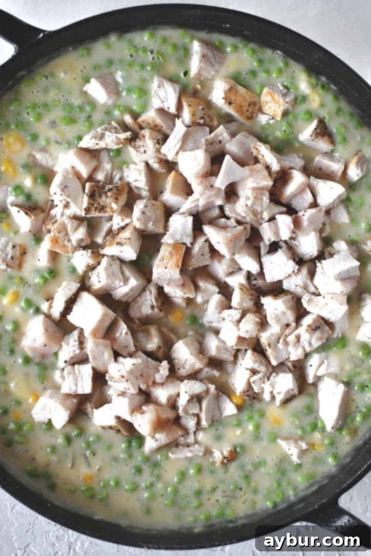 Golden Chicken Mash Bake 8 Adding diced chicken to the simmering sauce.