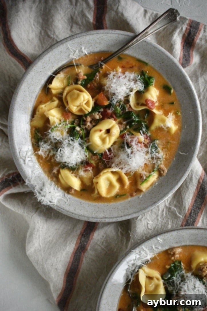Creamy Sausage Tortellini Soup in a bowl with topped with finely shaved parmesan, ready to eat.
