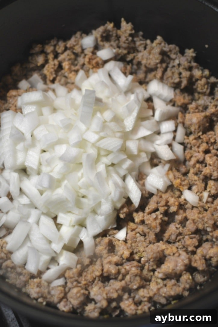 Adding the onions to the pot with the browned sausage to cook them till soft.
