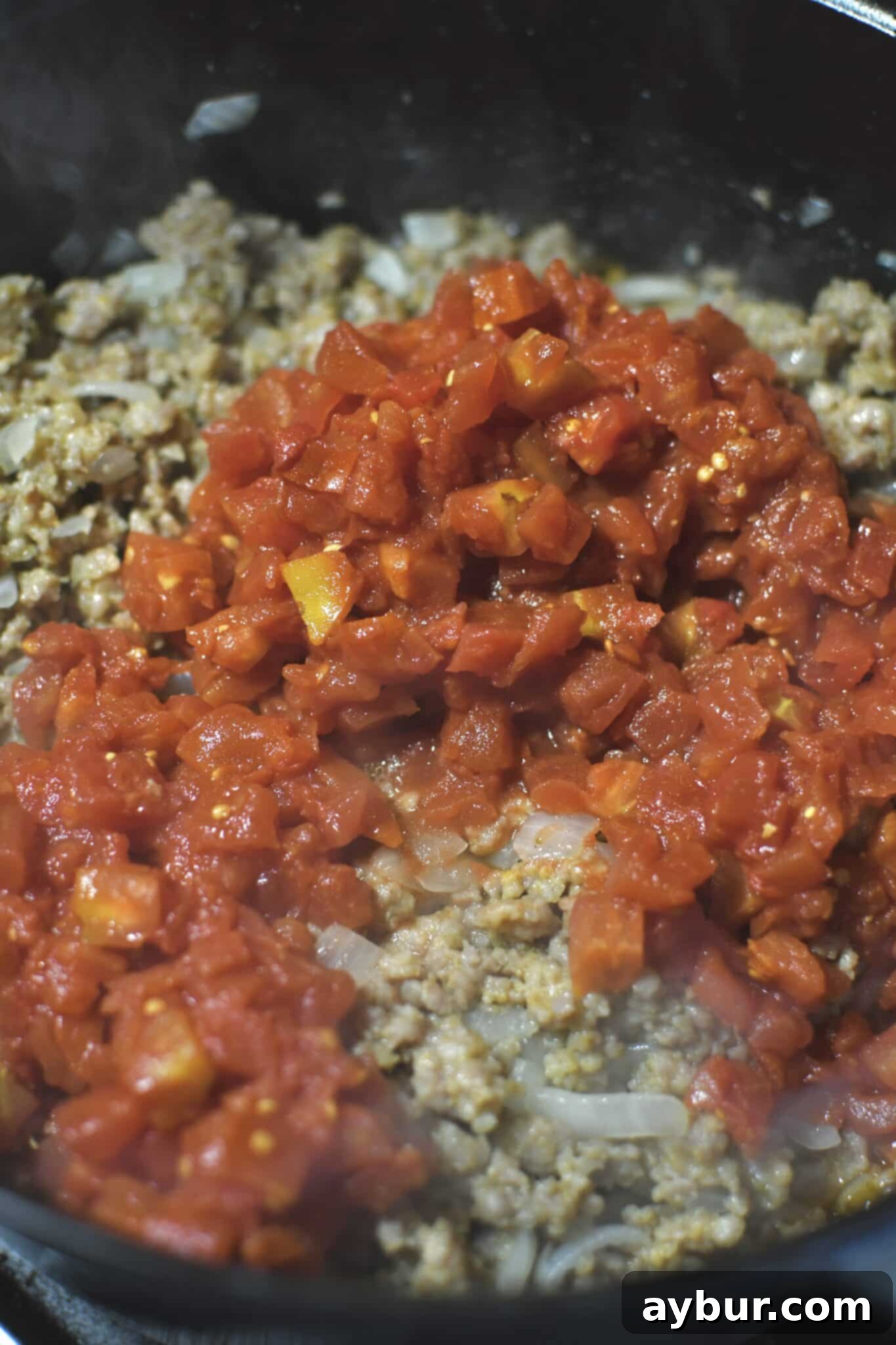 Adding the diced tomatoes and their juices to the soup pot over the cooked Italian sausage and onions.