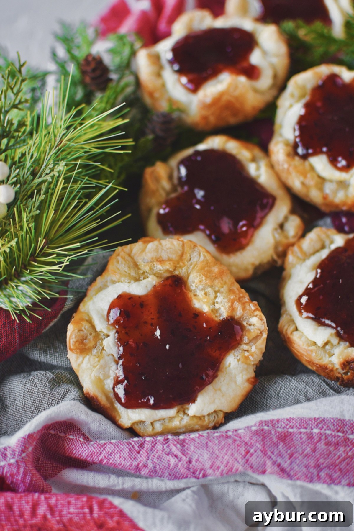A stunning shot of a Sugar Plum Cheese Danish gracefully placed on a Christmas-themed towel, adorned with fresh green foliage, evoking holiday warmth and deliciousness.