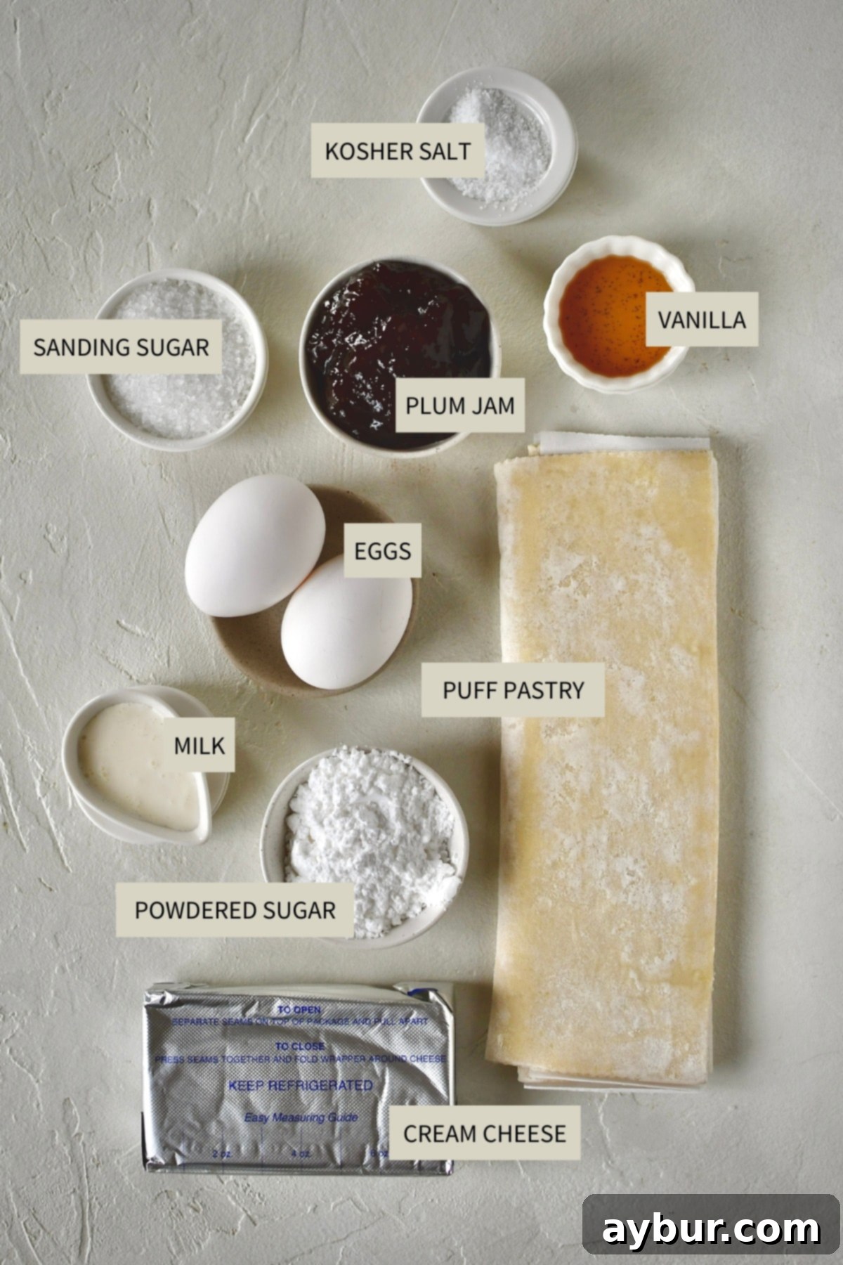 All the necessary ingredients laid out to prepare the delightful Sugar Plum Cheese Danish, including puff pastry, cream cheese, jam, and eggs.