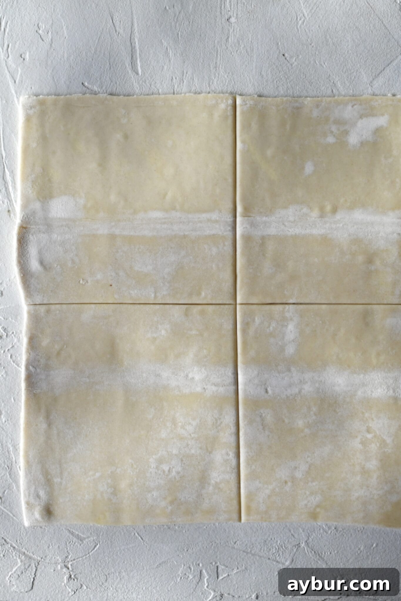 A sheet of puff pastry being carefully cut into four equal squares, preparing them for the danish folding process.