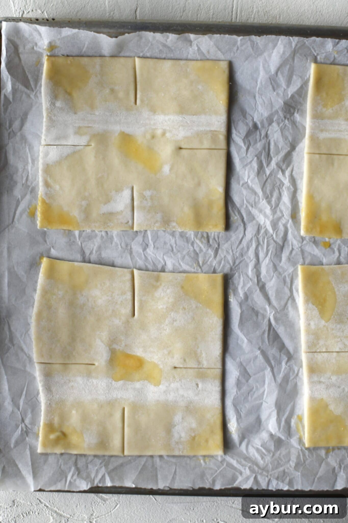 Puff pastry squares arranged on a baking sheet, with small dabs of egg wash strategically placed on each corner for folding and adhesion.