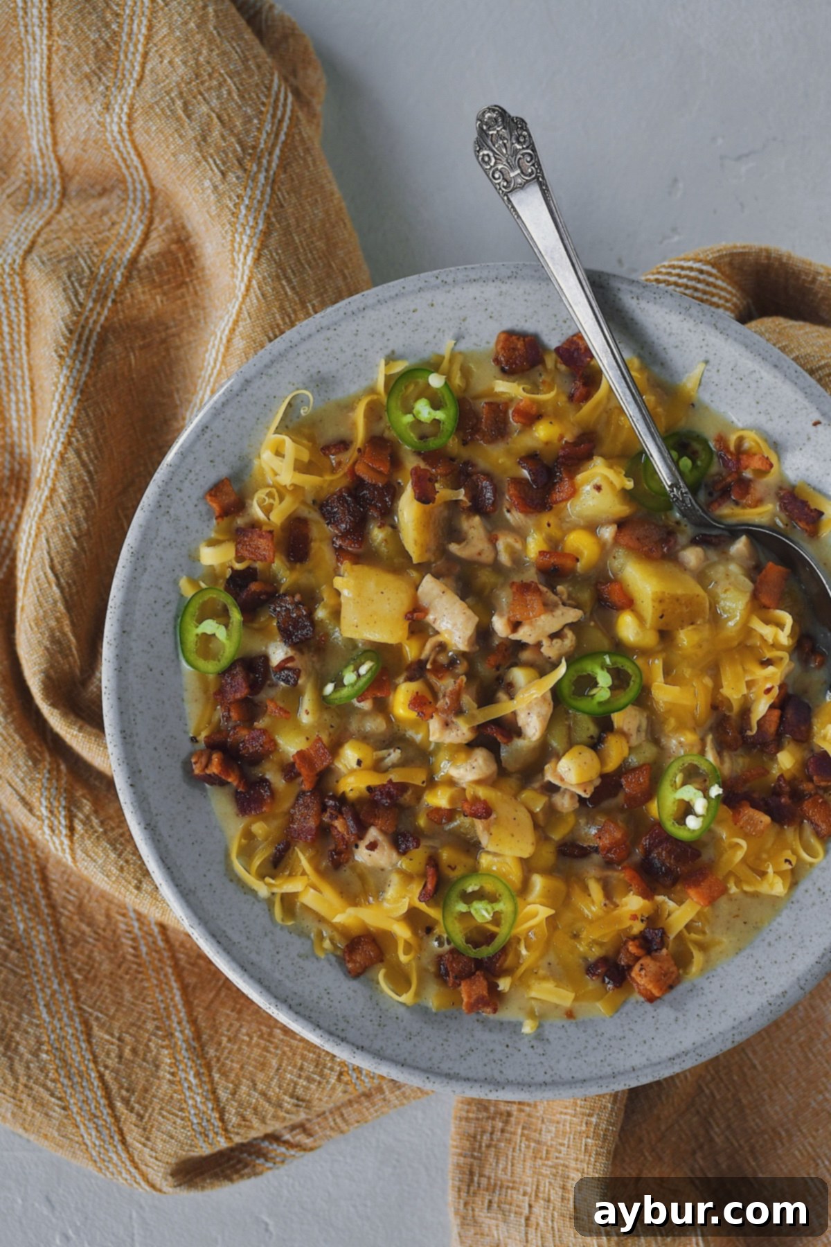 A bowl of rich Chicken Corn Chowder, generously topped with crispy bacon bits, melted cheddar cheese, and vibrant sliced peppers, ready to be enjoyed.