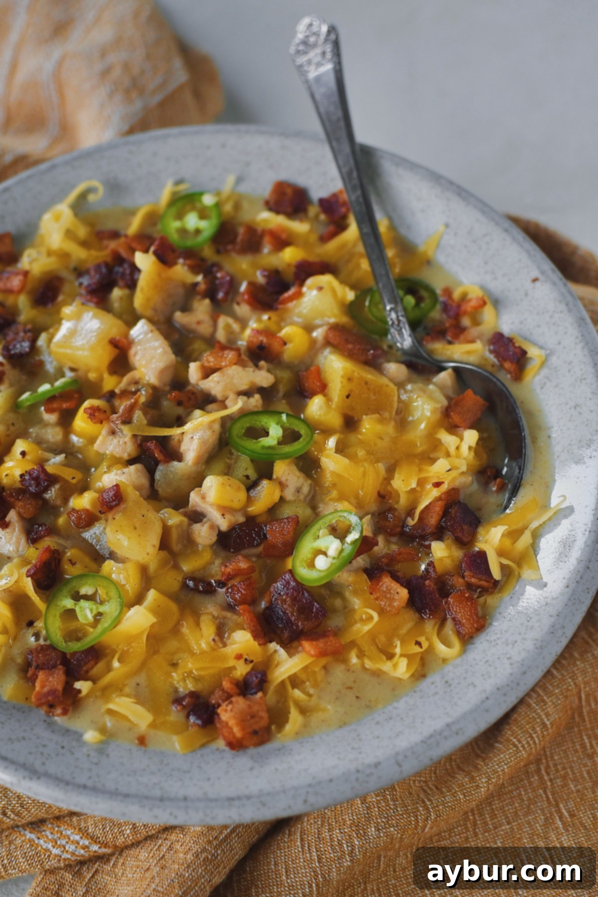A perfectly plated bowl of creamy Chicken Corn Chowder, garnished with fresh herbs, bacon, cheddar, and chili slices, ready for a cozy meal.