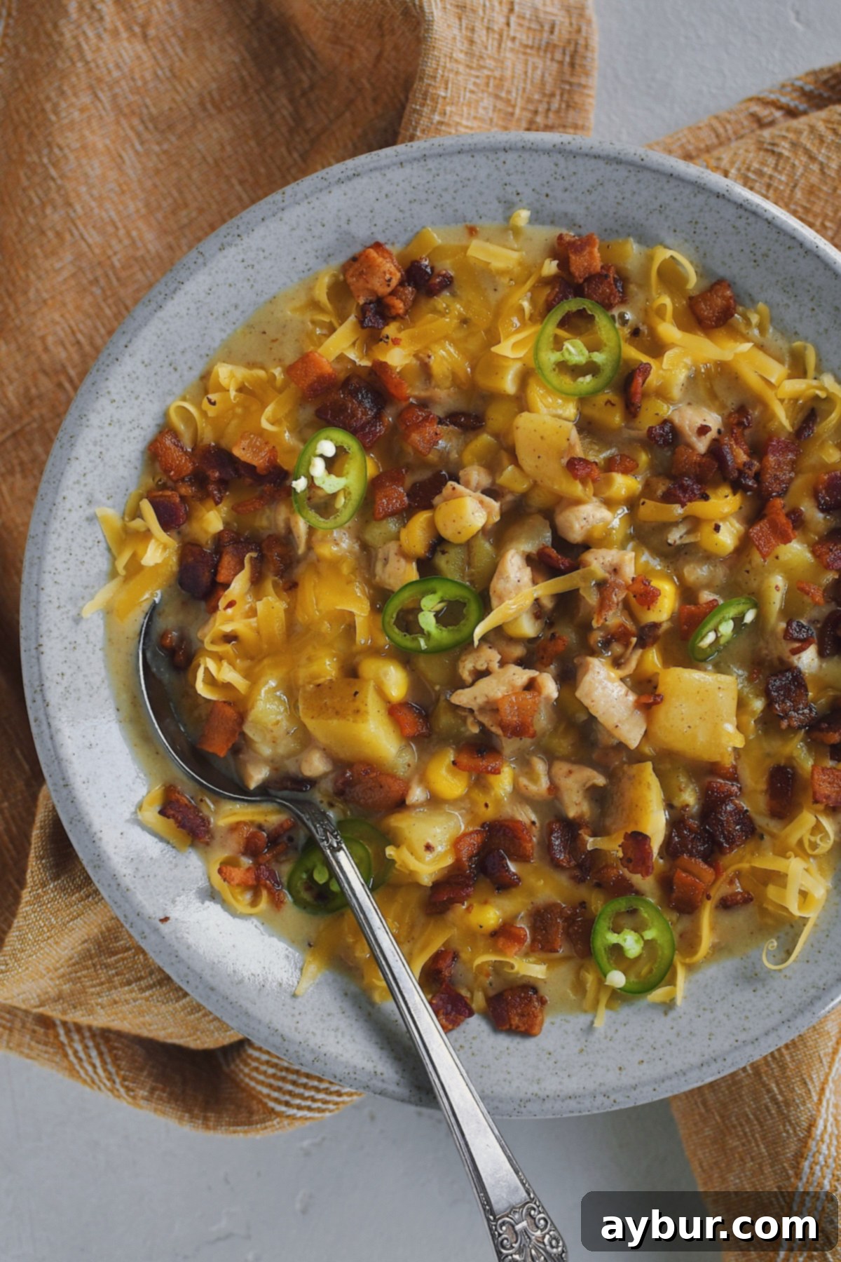 A close-up of a steaming bowl of Chicken Corn Chowder, showcasing its creamy texture and rich toppings, inviting a spoonful.