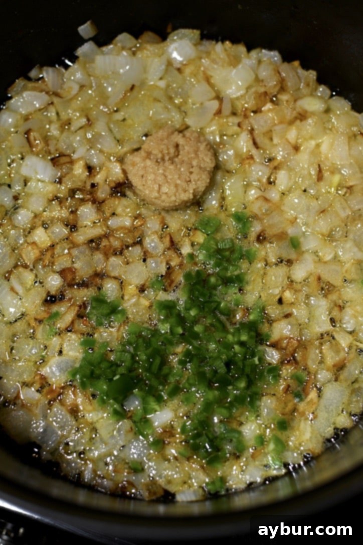 Minced garlic and diced serrano peppers being added to the softened, sautéed onions in the pot, infusing the base with aromatic flavors.