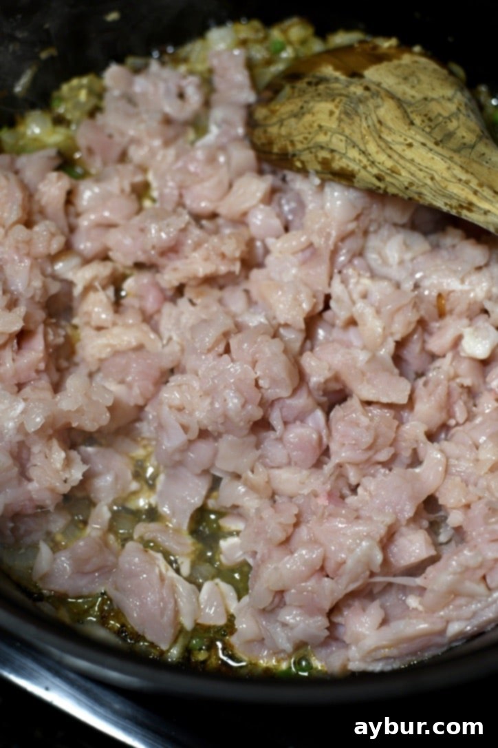 Finely diced chicken breast added to the pot with sautéed onions and garlic, beginning to cook.