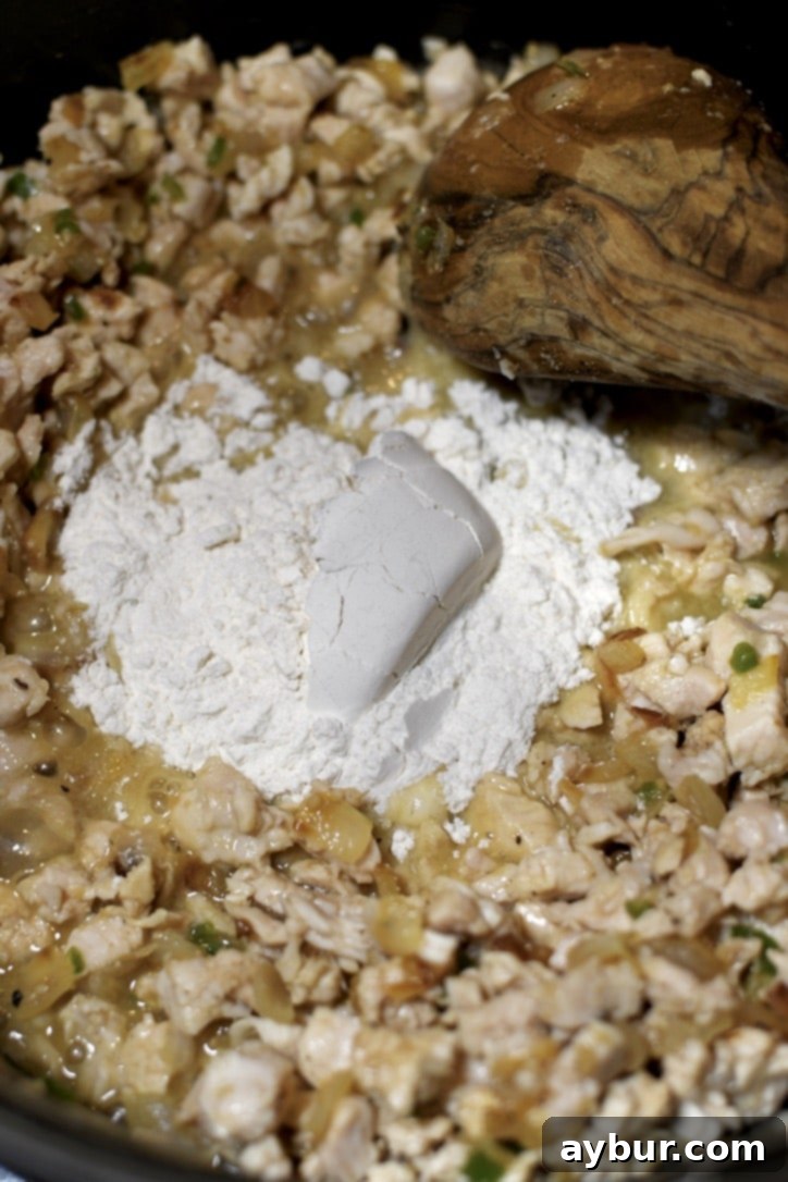 All-purpose flour being sprinkled over the cooked chicken and aromatics in the pot, ready to form a roux.