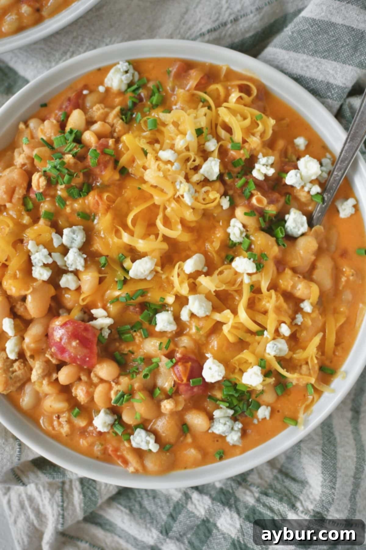 A bowl of creamy Buffalo Chicken Chili, garnished with a generous sprinkle of fresh chives, sharp blue cheese crumbles, and melted cheddar cheese.